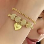 Gold bracelet with mesh beads and a glossy heart charm on wrist