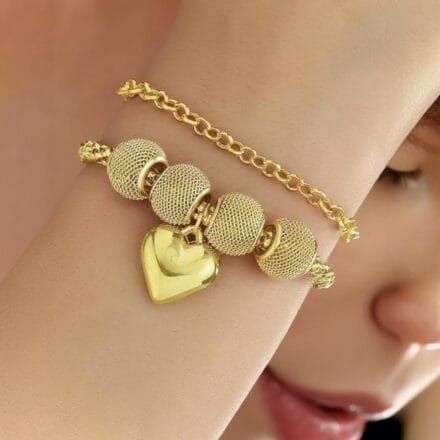 Gold bracelet with mesh beads and a glossy heart charm on wrist